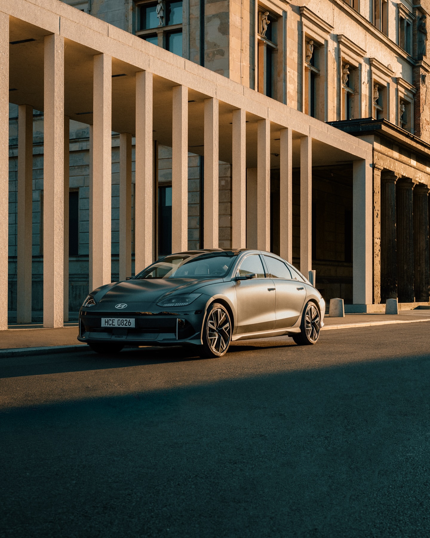 Dark gray Hyundai IONIQ 6 electric sedan parked on city street with modern architecture and warm lighting.