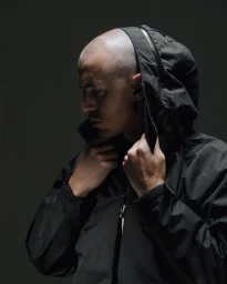 Portrait of a bald man adjusting the hood of a black waterproof jacket against a dark studio background
