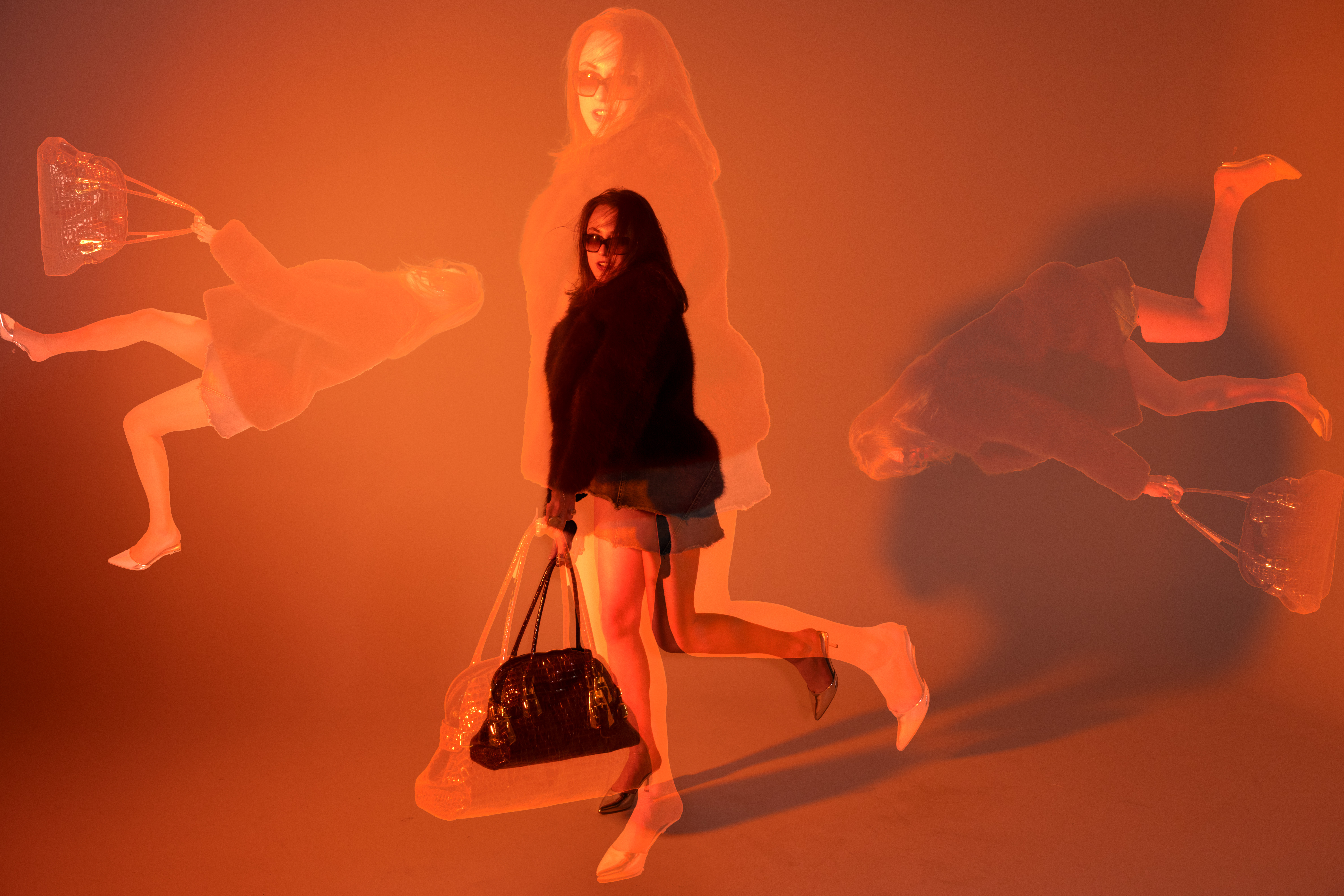 Multiple exposure fashion photograph of a woman in sunglasses holding a black handbag against an orange lit background by Violet Johnston.