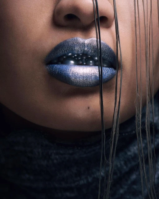 Close-up portrait of an adult woman with a dark complexion, wearing dark blue lipstick and black hair strands over her face.