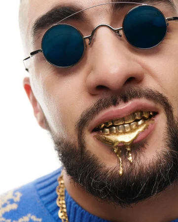 Close-up of an adult male wearing sunglasses and a gold grill, with a gold chain visible, against a bright white background.