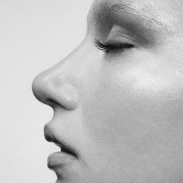 Black-and-white close-up of a woman's face, showing the side profile of her nose, lips, and closed eye, with soft lighting.