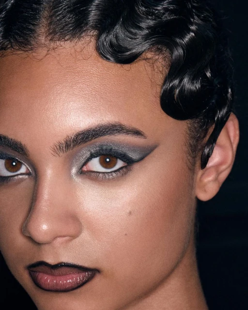 Close-up portrait of a woman with dramatic eye makeup and glossy lips in a dimly lit setting, showcasing beauty and cosmetic art.