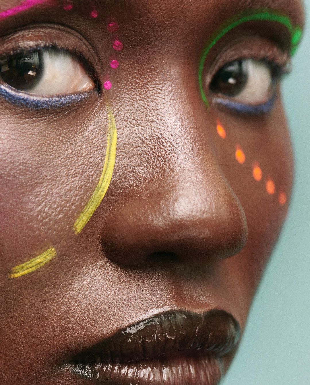 Close-up portrait of a Black woman with colorful face paint in a studio setting, highlighting beauty and artistic expression.