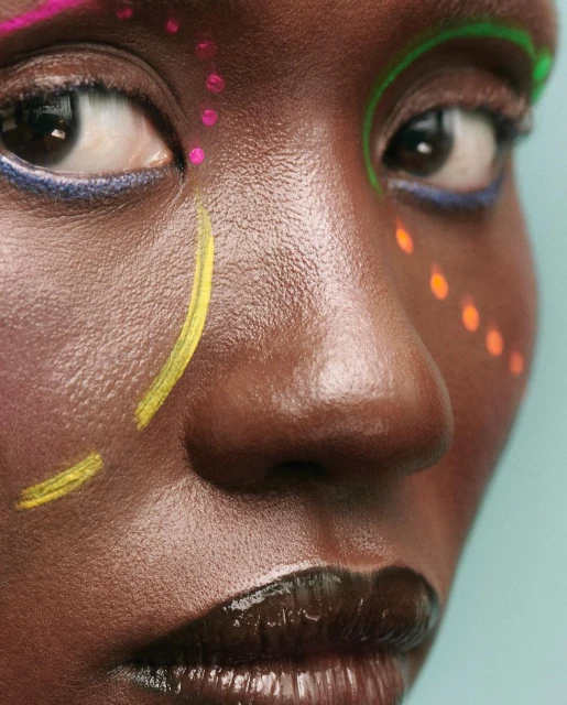 Close-up portrait of a Black woman with colorful face paint in a studio setting, highlighting beauty and artistic expression.