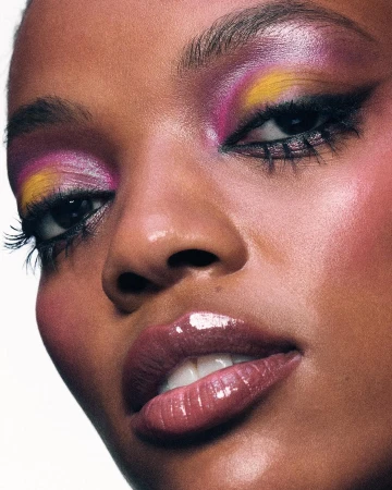 Extreme close up portrait of a Black woman with vibrant pink and yellow eyeshadow and glossy lips
