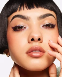 Close-up beauty portrait of a woman with short black hair and defined eye makeup touching her face against a white background