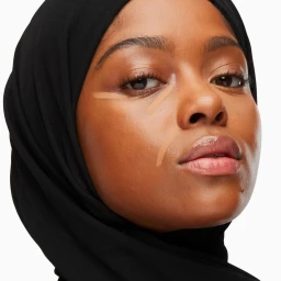 Close-up beauty portrait of a Black woman wearing a black hijab with concealer stripes on her cheeks, photographed by Marion Clémence Grand.