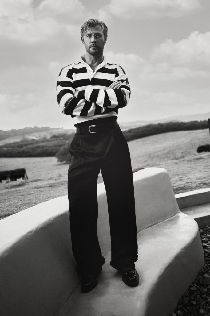 Chris Hemsworth standing outdoors in a striped rugby shirt and wide-leg trousers in black and white