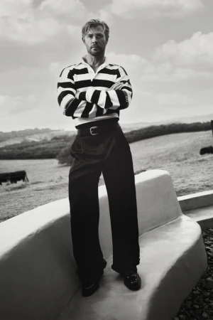 Chris Hemsworth standing outdoors in a striped rugby shirt and wide-leg trousers in black and white