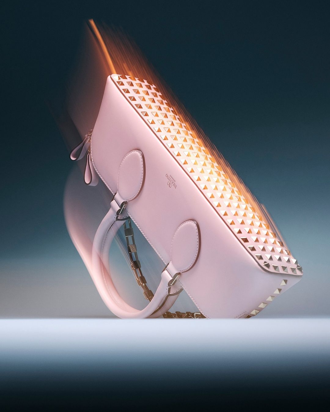 Elegant pink leather purse with gold pyramid stud embellishments and a gold chain, shot in a studio with dynamic motion blur.