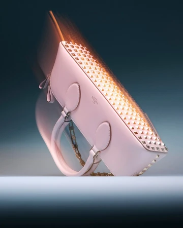 Elegant pink leather purse with gold pyramid stud embellishments and a gold chain, shot in a studio with dynamic motion blur.