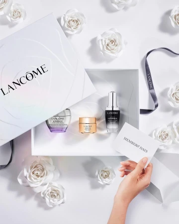 Cosmetic product set by Lancôme in a white gift box with white paper flower decorations, against a bright white background.