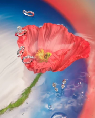 Diamond rings and earrings floating around a vibrant red poppy flower submerged in swirling blue and red water.