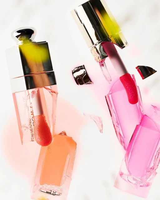 Product shot of two lipstick containers, one filled with peach-colored lipstick and the other with pink, on a white surface.