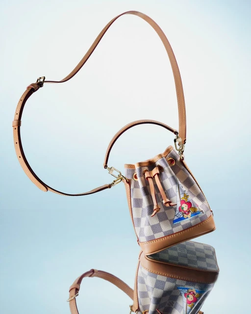 Upscale bucket bag featuring a checkerboard pattern and whimsical cartoon character graphic, paired with a tan leather strap on a light gradient.
