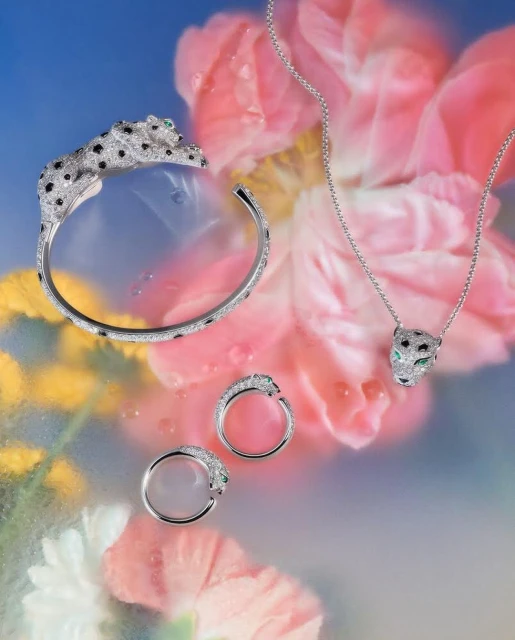 Elegant jewelry set featuring a bangle, a ring, and a necklace with panther designs, set against a backdrop of soft floral patterns.