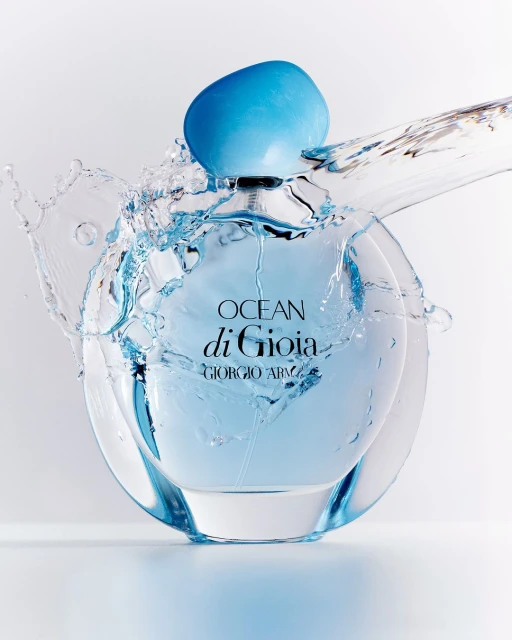 Close-up of a clear, round Giorgio Armani Ocean di Gioia perfume bottle with a blue cap, surrounded by a splash of clear water against a white background.