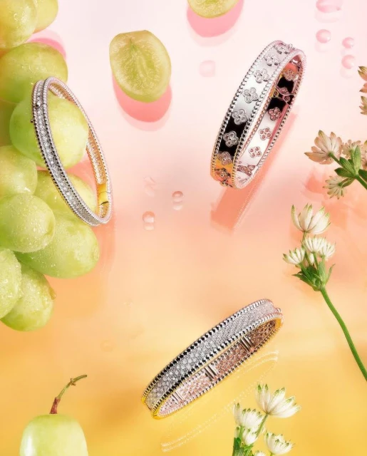 Three diamond bangles are showcased with green grapes and white flowers against a gradient peach and yellow background, high angle view.