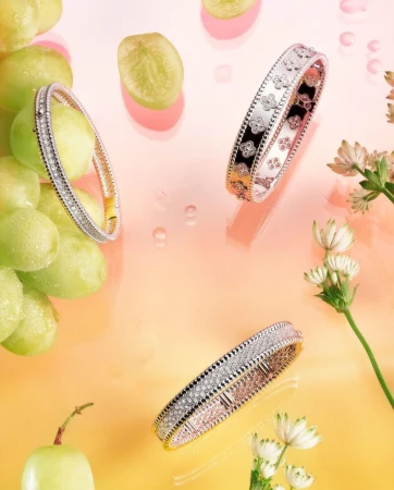 Three diamond bangles are showcased with green grapes and white flowers against a gradient peach and yellow background, high angle view.