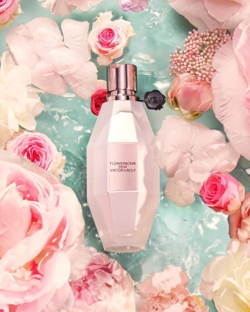 Flowerbomb Dew Viktor&Rolf fragrance bottle surrounded by pink and white flowers floating in light blue water, creating a serene beauty scene.