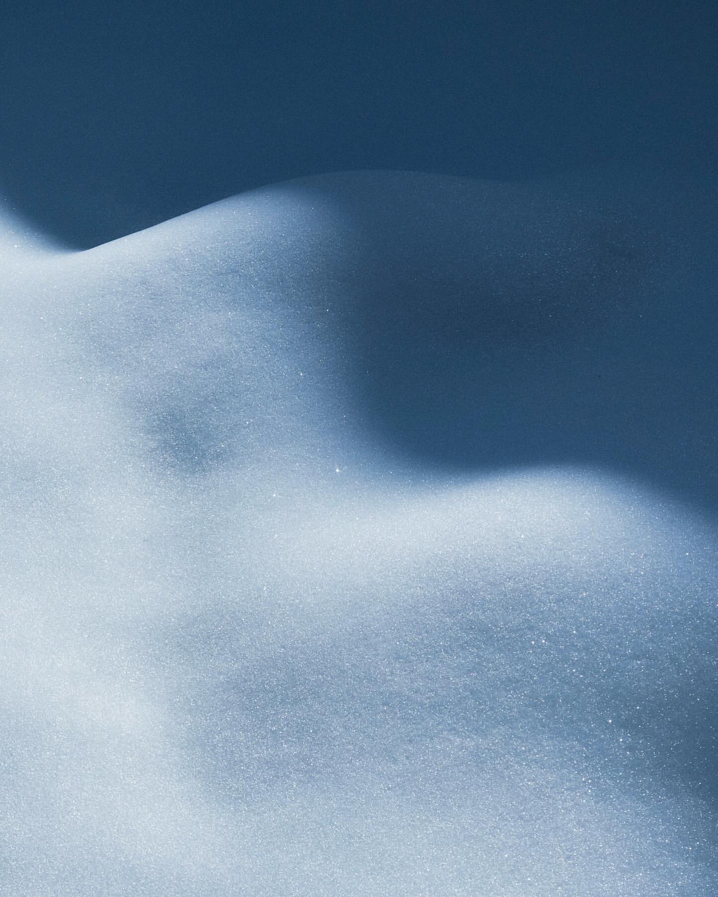 Undulating snowy landscape in soft cool hues, featuring light and shadow play on snow drifts and mounds, in a minimalistic composition.
