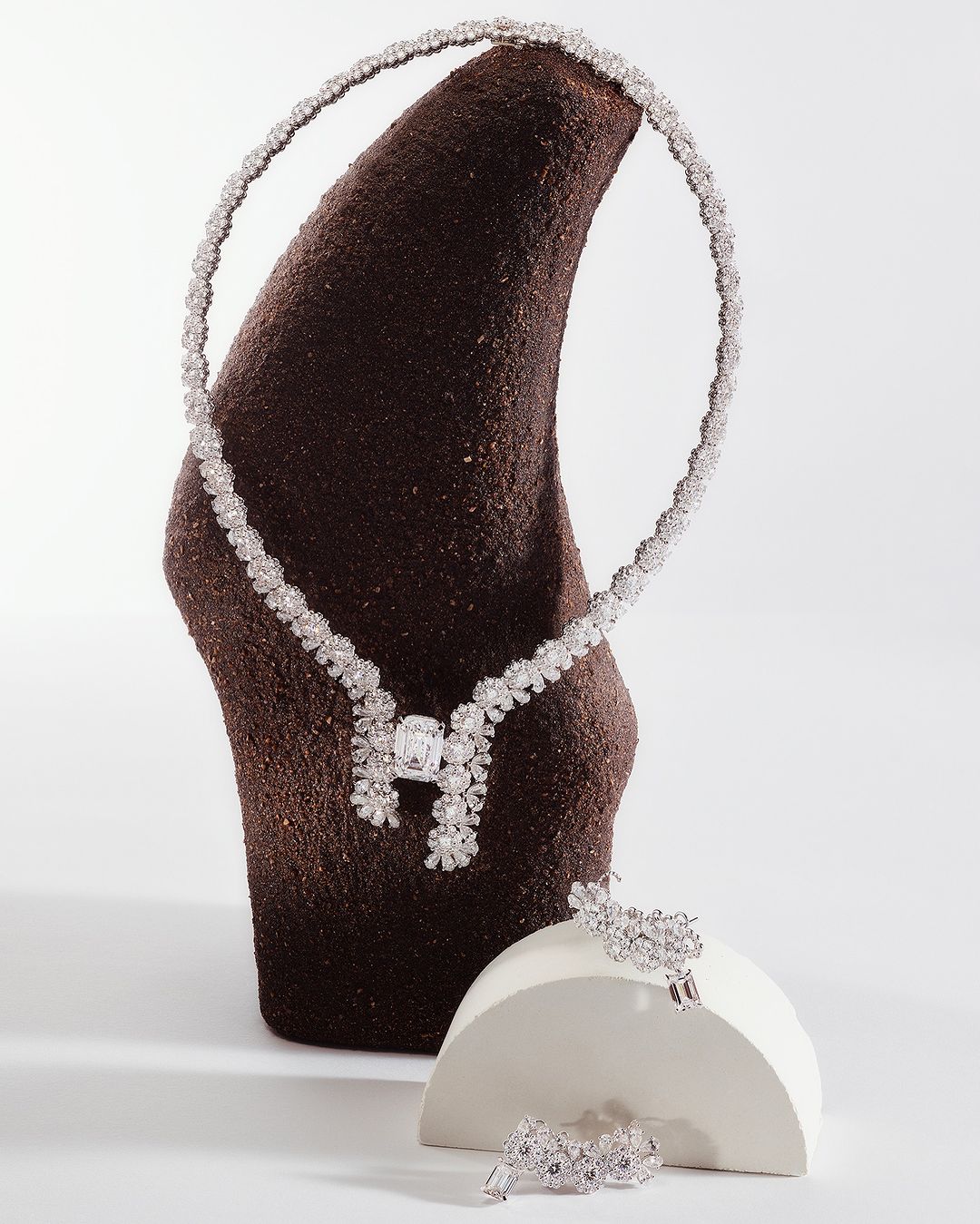 Elegant floral diamond necklace and jewelry set displayed on modern sculpted pedestals against a neutral background in a studio setting.