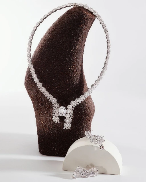 Elegant floral diamond necklace and jewelry set displayed on modern sculpted pedestals against a neutral background in a studio setting.