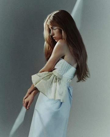 Portrait of a woman with long hair wearing a strapless top and light skirt against a wall with a diagonal streak of light