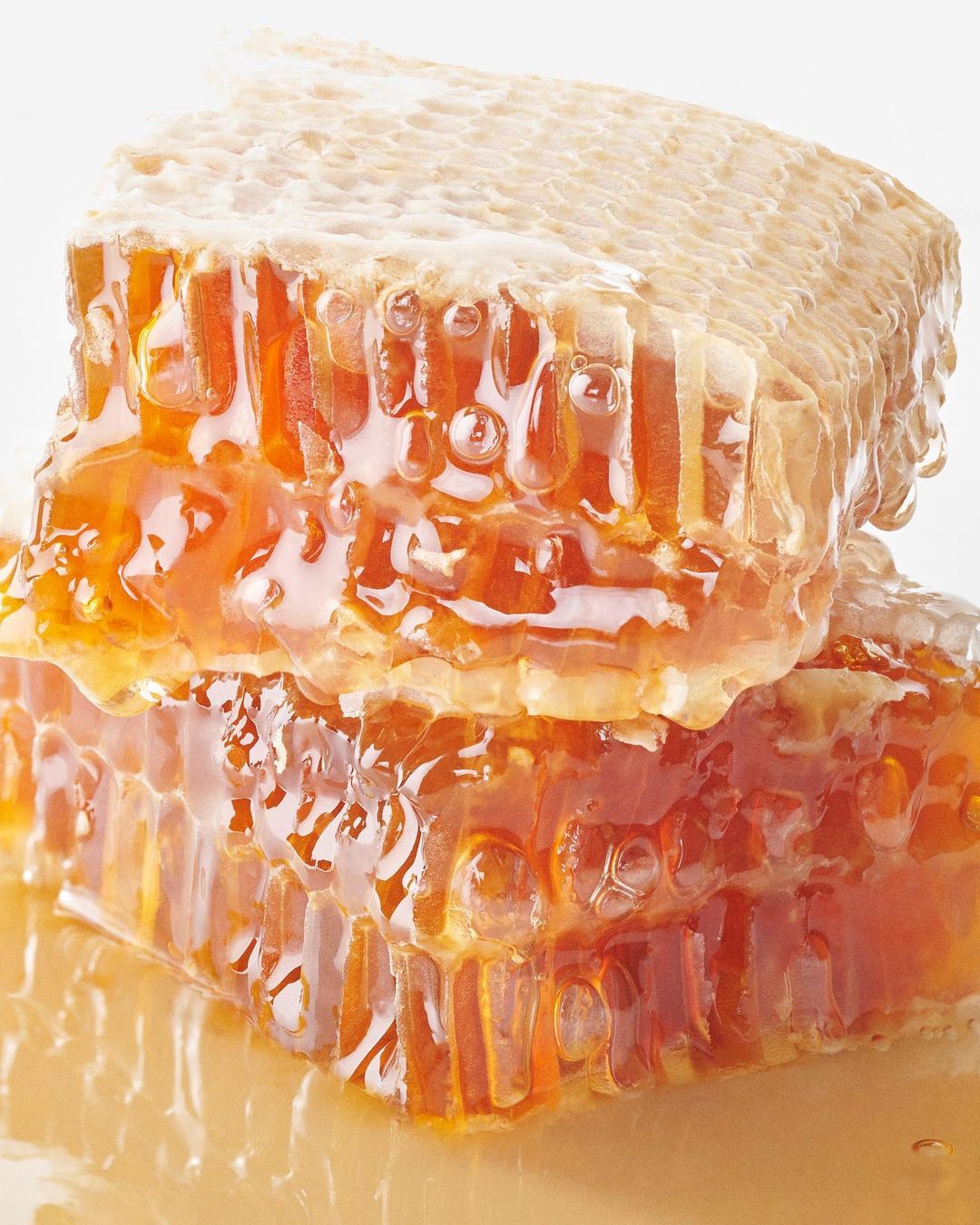 Close-up still life of a stacked honeycomb with dripping honey against a white background, product photography, food photography, focus shot.