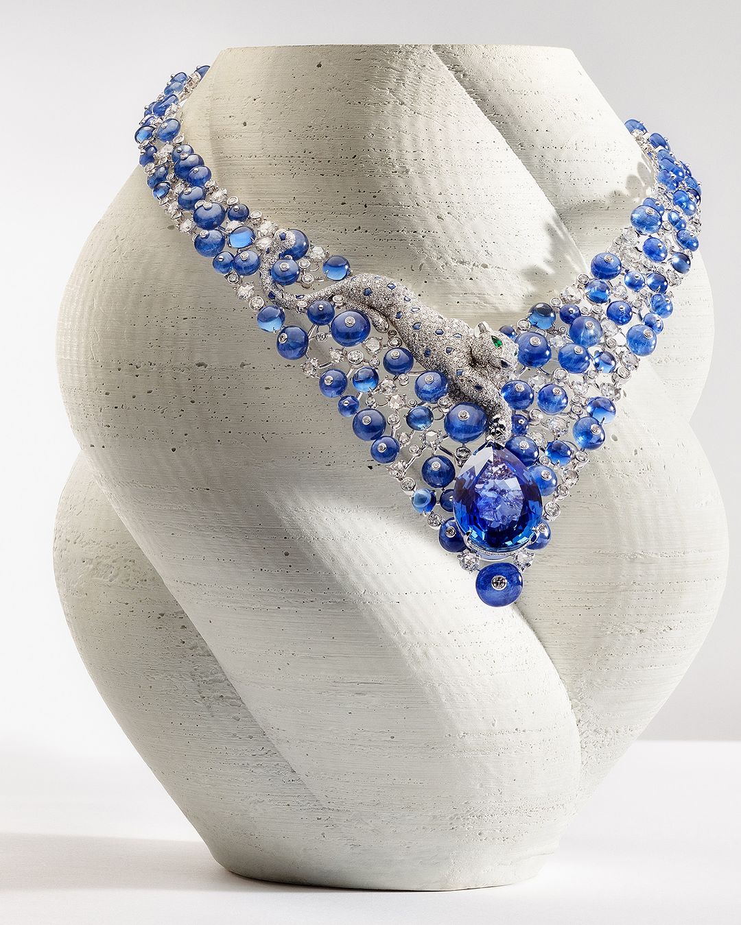 A stunning sapphire and diamond necklace with a panther design, displayed on a textured, organic bust in a studio setting.