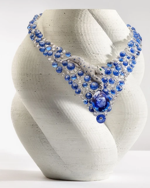 A stunning sapphire and diamond necklace with a panther design, displayed on a textured, organic bust in a studio setting.