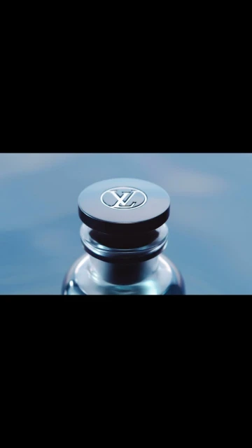 Close-up of a perfume bottle featuring the Louis Vuitton logo on its dark-colored cap against a blurred, dark blue background.