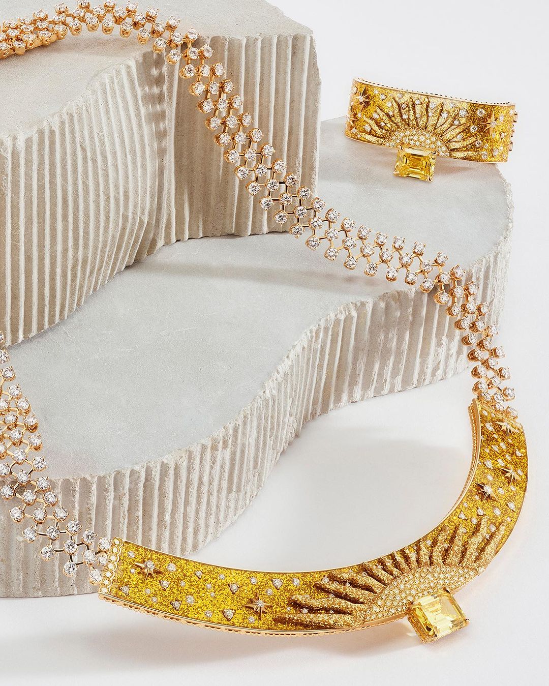Gold necklace and bracelet jewelry set with yellow gemstones and diamonds on a textured white background for luxury jewelry presentation.