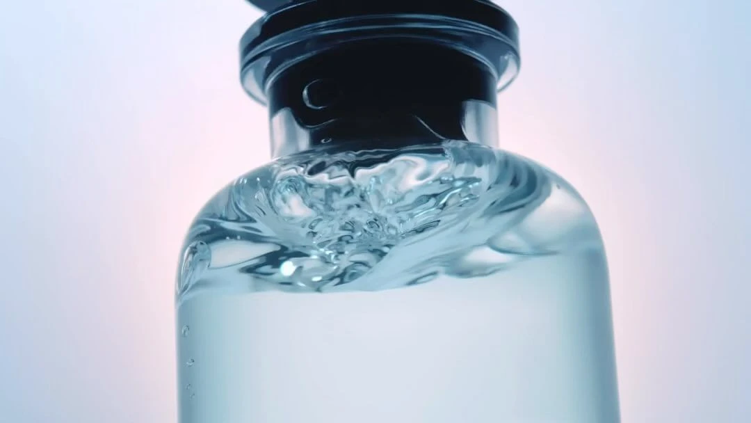 Close-up shot of a clear glass bottle with a black top, filled with swirling, transparent liquid against a light background.