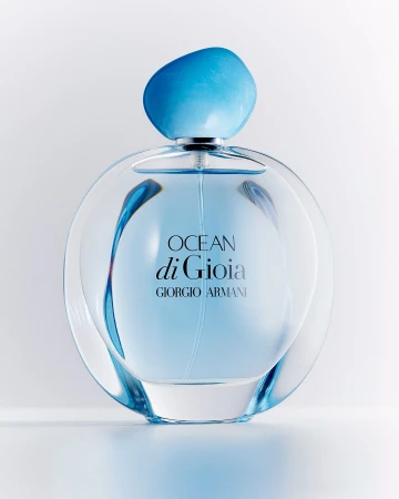Round glass perfume bottle with blue liquid and organic shaped blue cap on white background
