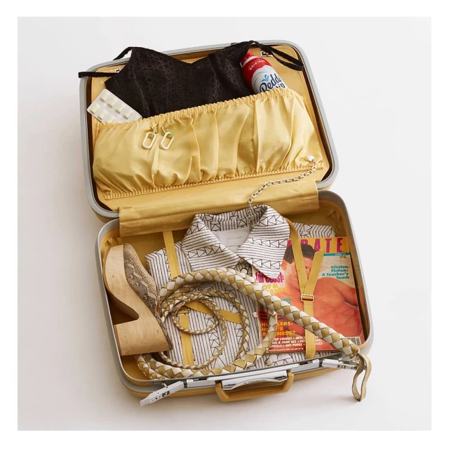 Open vintage suitcase packed with women's clothing, shoes, and accessories arranged neatly on a white surface with soft lighting.