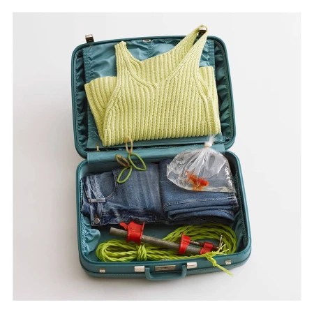 Open blue suitcase packed with clothing, rubber bands, workout equipment and a gold fish in a plastic bag on a white background.