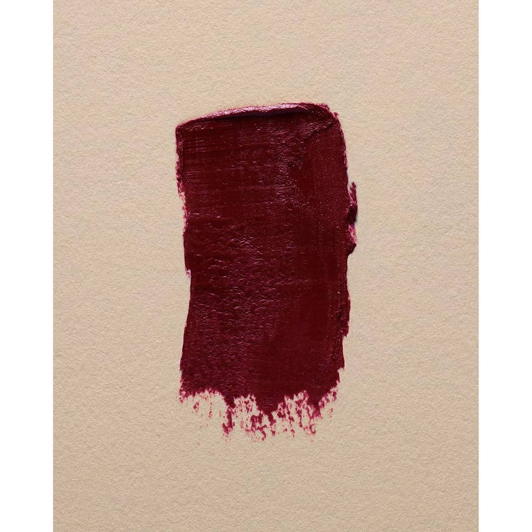 Deep burgundy lipstick swatch on textured beige paper surface photographed by Marius W Hansen