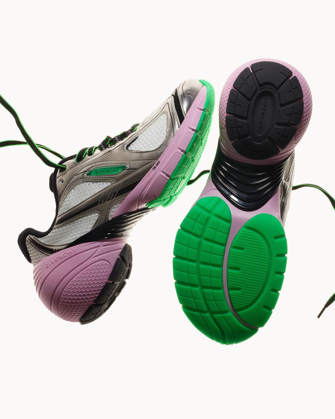 Two Givenchy running shoes are displayed against a white backdrop, showing the sole tread and design details with green and pink accents.