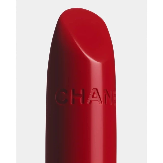 Macro shot of red Chanel lipstick with visible logo against an off-white background, showcasing beauty and cosmetic product photography.