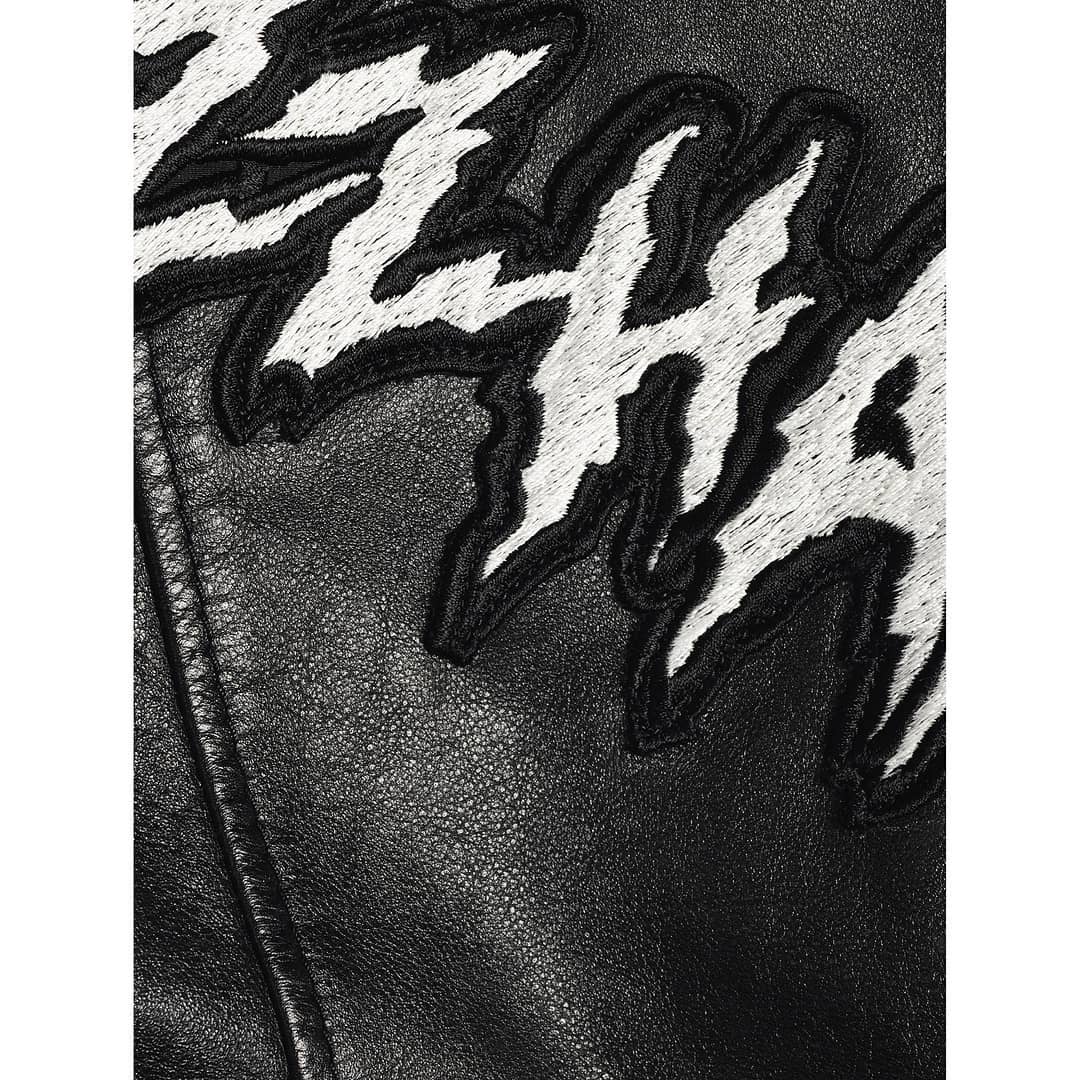 Close-up of a black leather jacket featuring white embroidered designs with a textured and detailed view, emphasizing fashion and style.