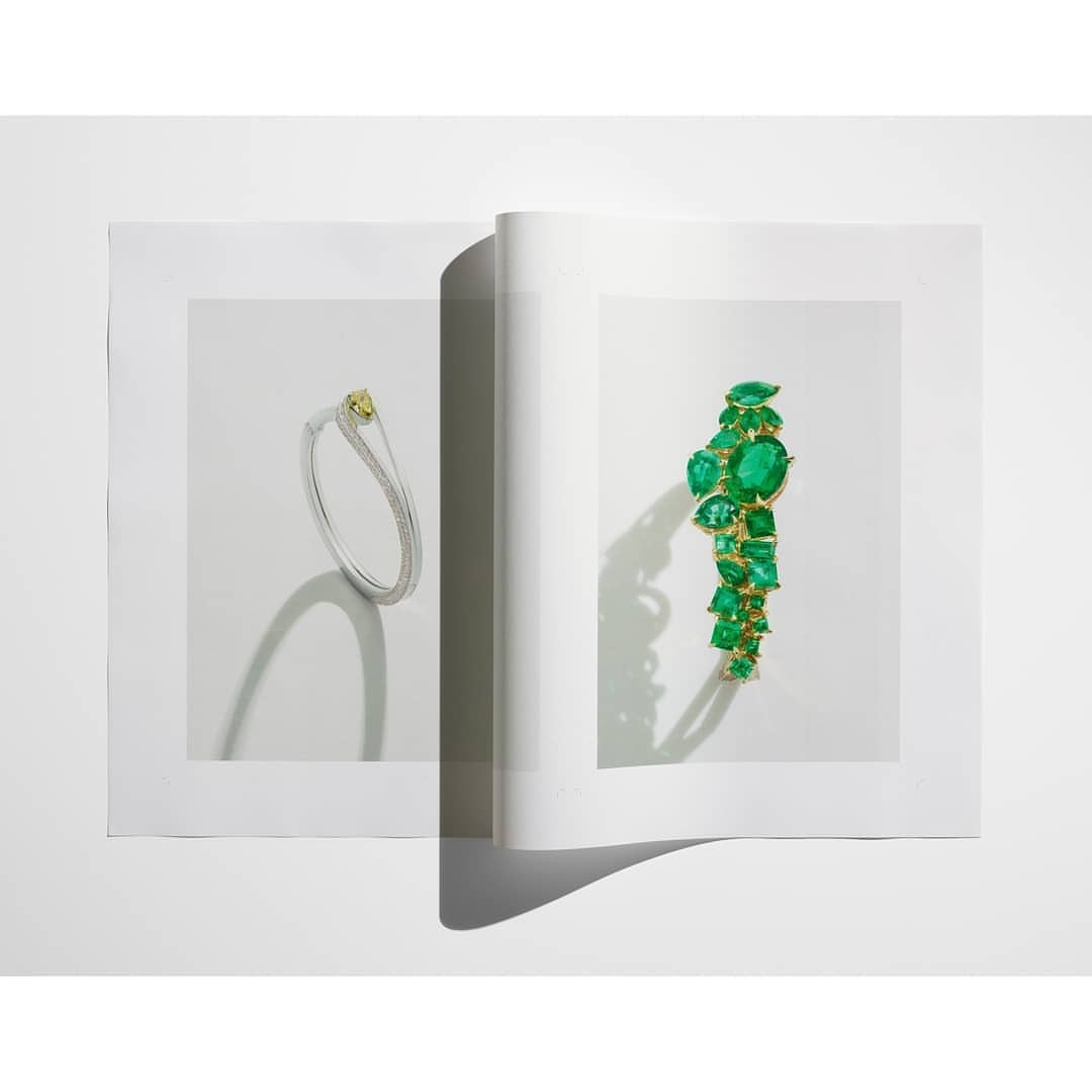 Open magazine spread features a yellow and diamond bracelet plus an emerald and gold bracelet, jewelry advertisement, indoor shot.