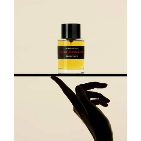 A perfume bottle resting on a black surface above a silhouetted hand touching the underside of the ledge.