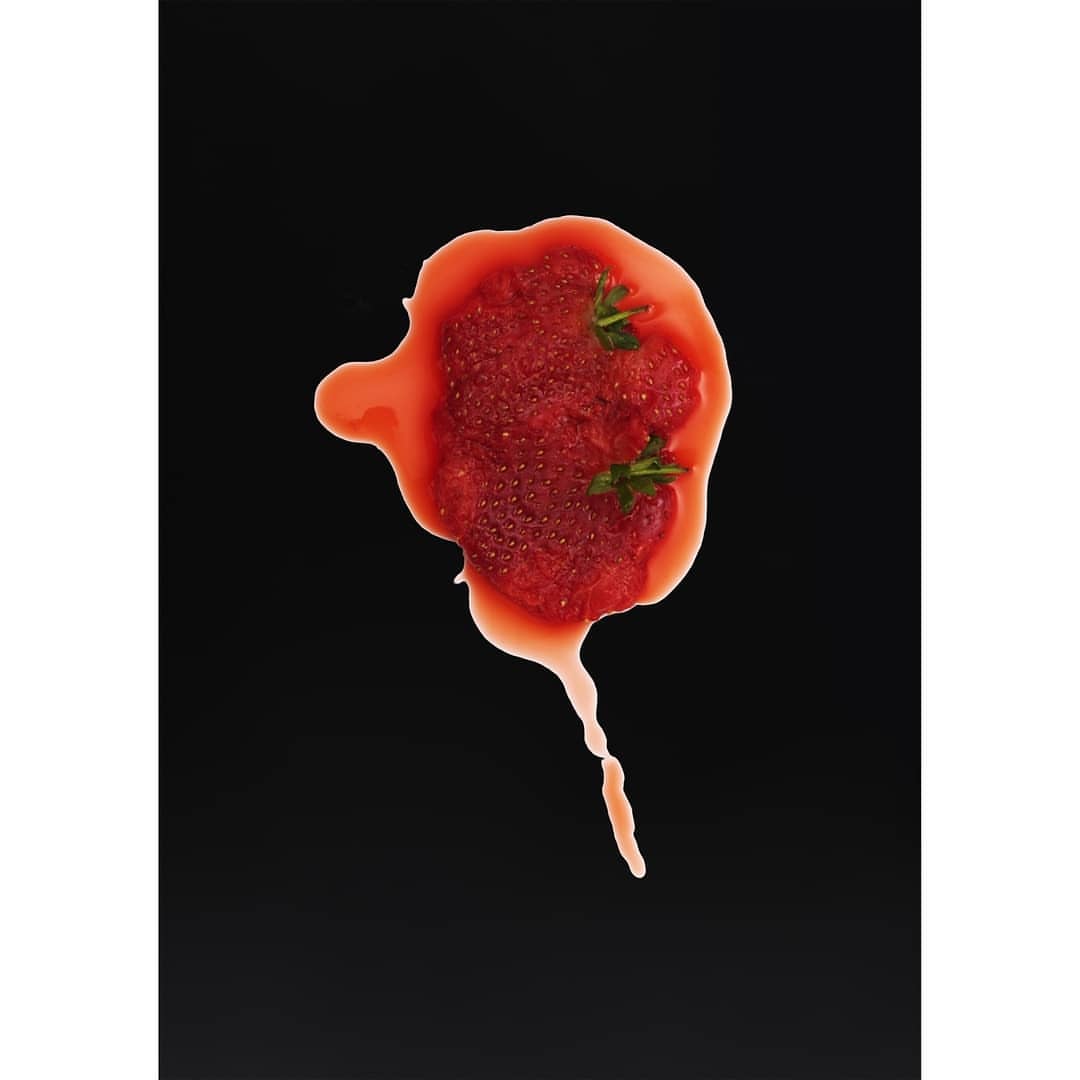 Overhead shot of strawberry puree with green sprigs on a black surface, offering a vibrant contrast of red and green.