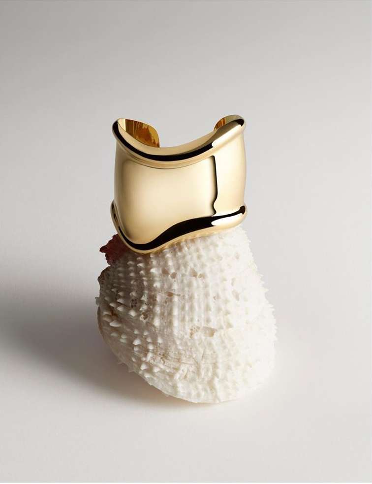 Close-up of a gold bracelet on a textured white sea urchin against a white backdrop, jewelry display, studio lighting.
