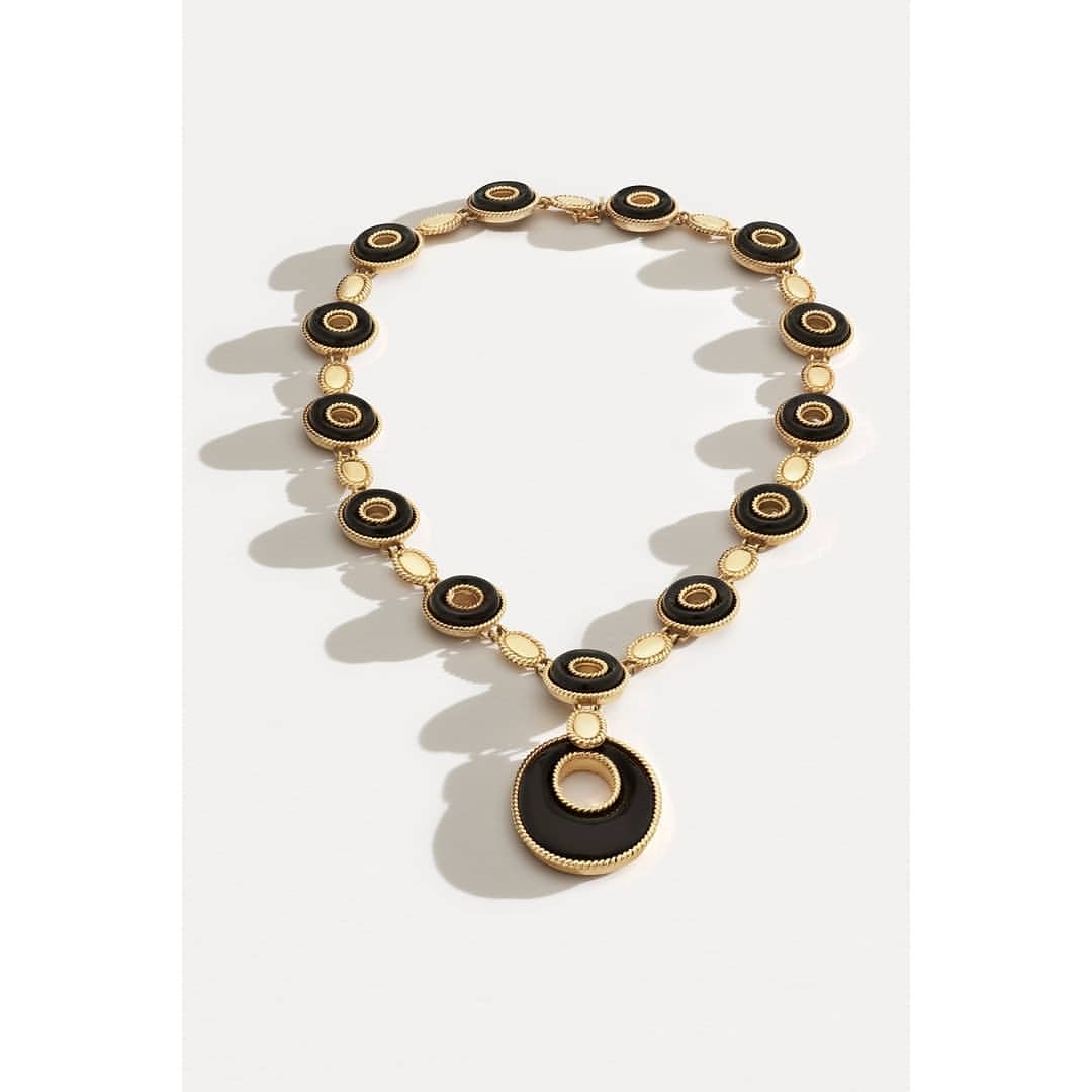 Elevated shot of a gold necklace with circular black and gold charms on a white surface, creating a visually appealing jewelry product shot.
