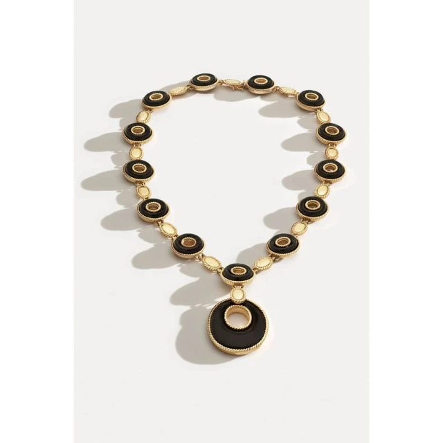 Elevated shot of a gold necklace with circular black and gold charms on a white surface, creating a visually appealing jewelry product shot.