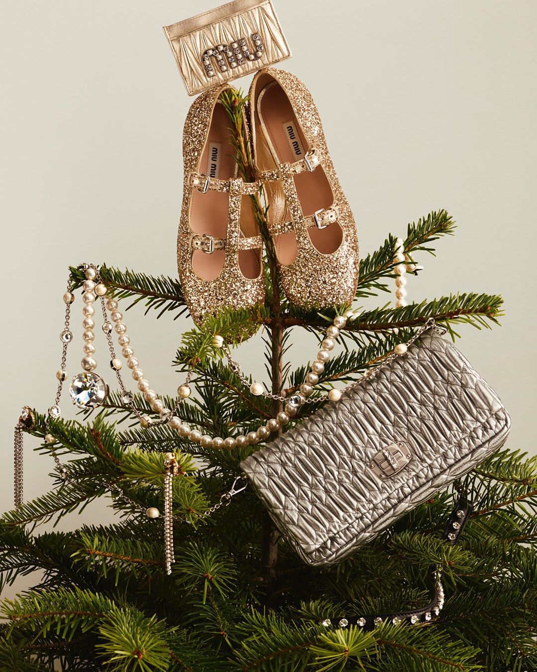 Festive fashion still life featuring Miu Miu flats and handbags arranged on a Christmas tree, accessorized with pearl necklaces.