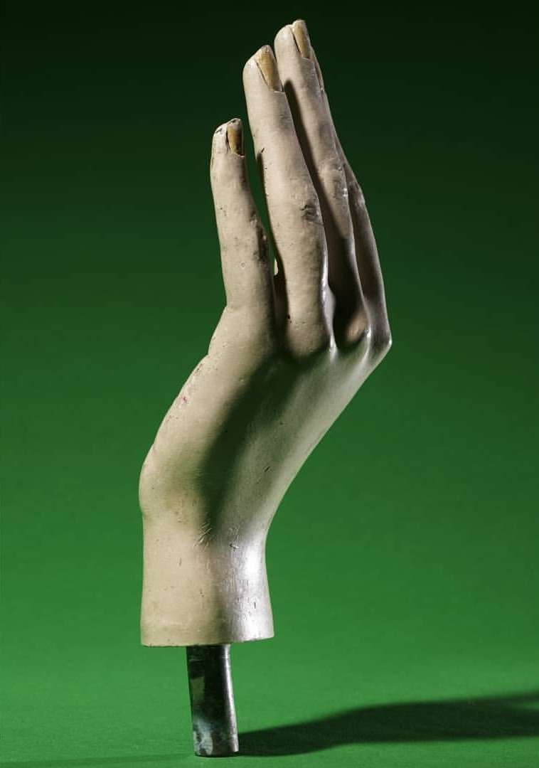 Artistic studio shot of a mannequin hand with raised fingers against a vibrant green backdrop, emphasizing its sculptural form and texture.
